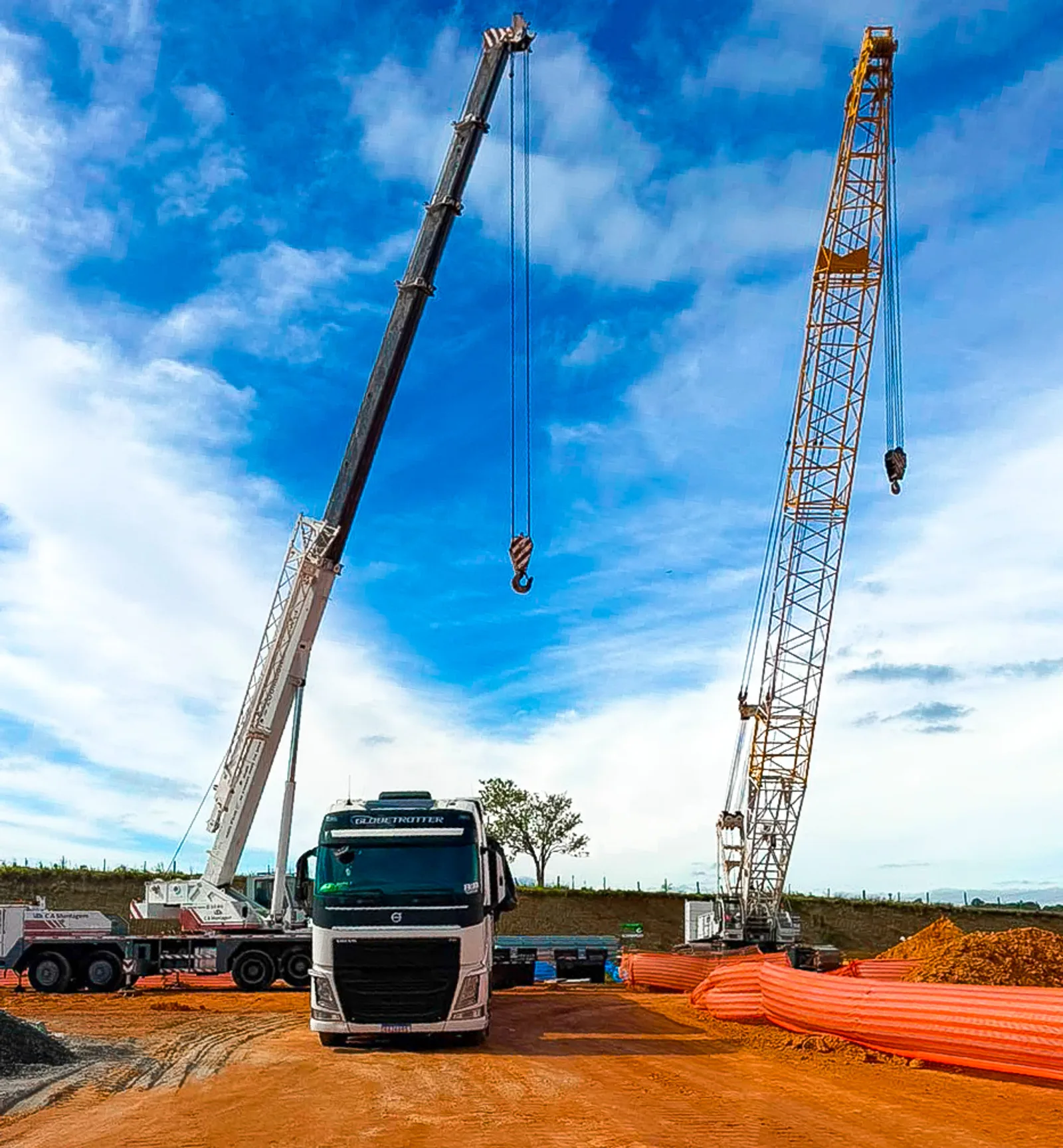 Caminhão da R&B Transportes em canteiro de obra ao lado de guindastes